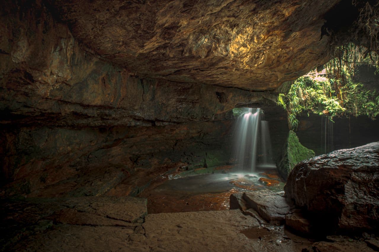 Explorer standing at the mouth of a limestone cave in Meghalaya with light streaming into the dark passage