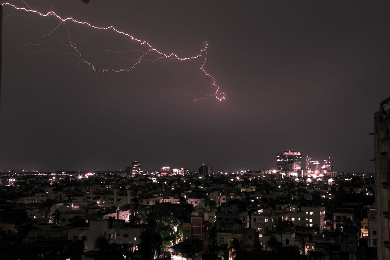 Evening thunderstorm with lightning bolt over a city skyline at dusk during pre-monsoon season in India